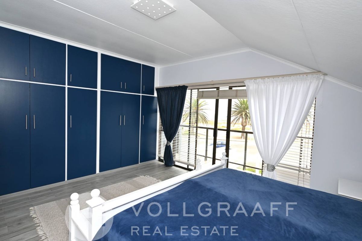 A bright bedroom featuring extensive built-in navy blue cabinetry, modern grey flooring, and large sliding glass doors leading to a balcony.