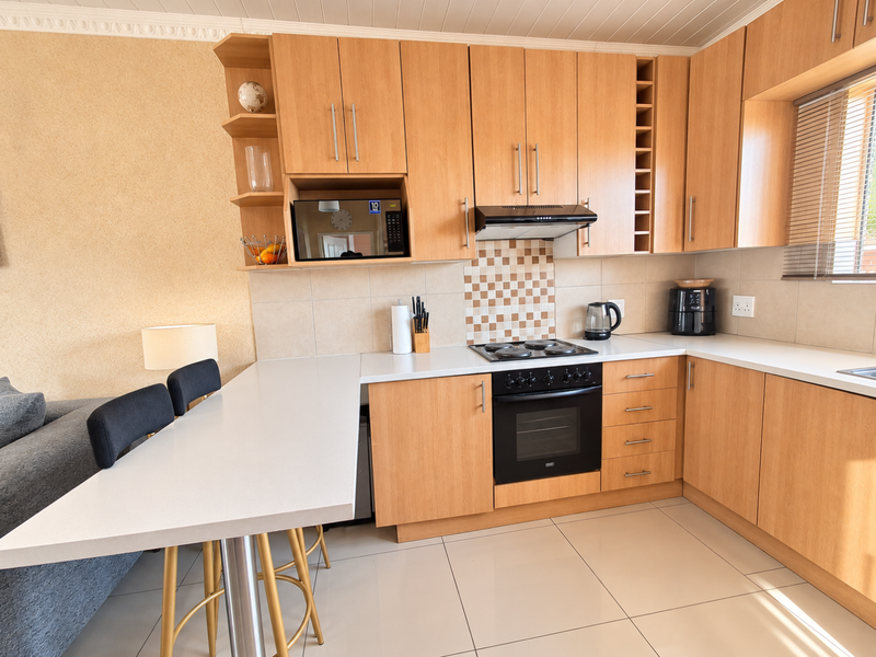 Open-plan kitchen featuring light wood cabinetry, laminate countertops, built-in oven, hob, and a breakfast bar, seamlessly integrated with the living area.