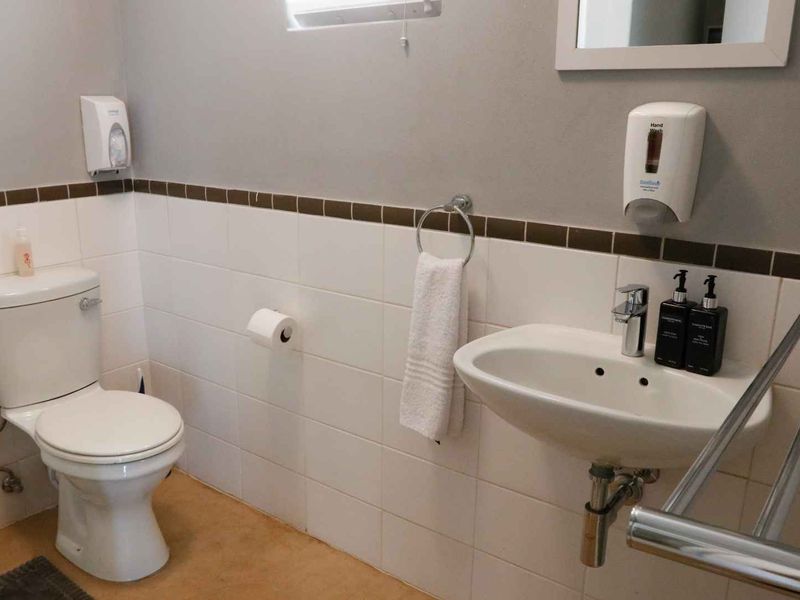 A functional bathroom featuring a white toilet, wall-mounted basin with chrome tapware, and tiled splashback with decorative border.