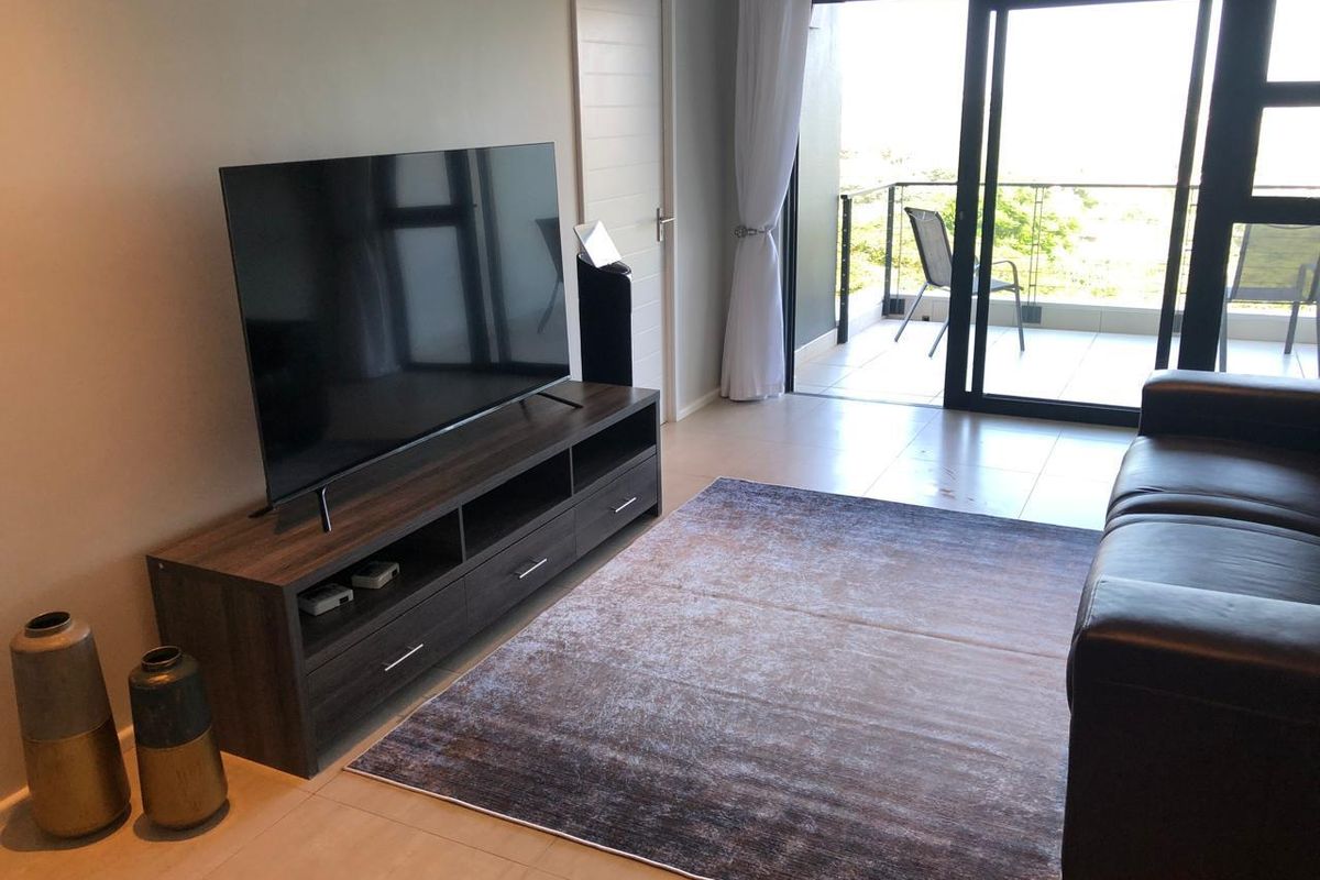 A bright living room featuring tiled flooring and large sliding glass doors that open onto a private balcony with outdoor seating.