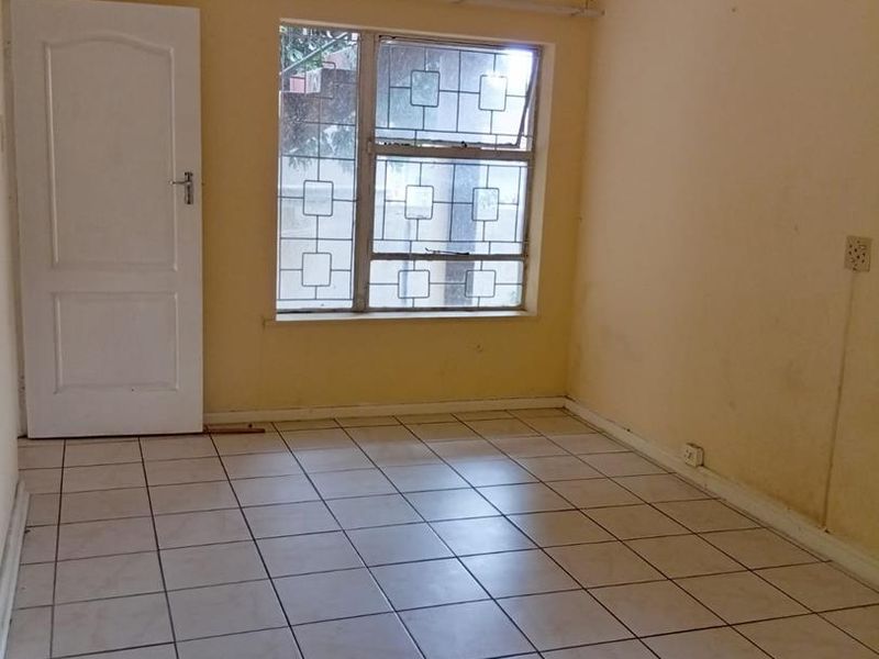 An empty bedroom featuring tiled flooring, a ceiling fan, and security bars on the window, requiring cosmetic updates to the wall finishes.