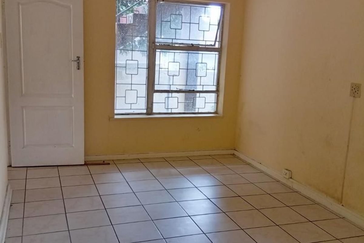 An empty bedroom featuring tiled flooring, a ceiling fan, and security bars on the window, requiring cosmetic updates to the wall finishes.