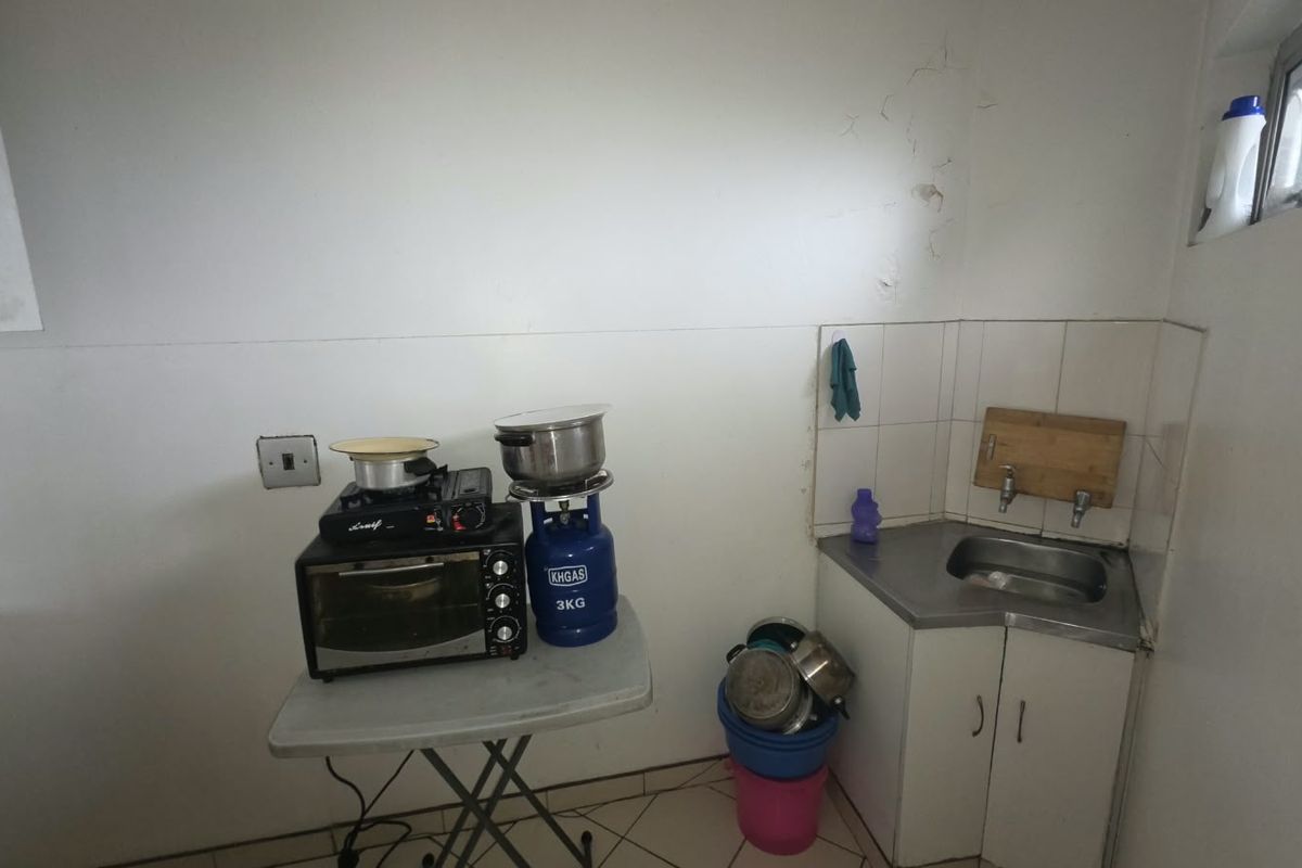 A compact kitchen area featuring a corner sink, tiled splashback, and built-in cabinetry, requiring some maintenance and cosmetic updates to the wall finishes.