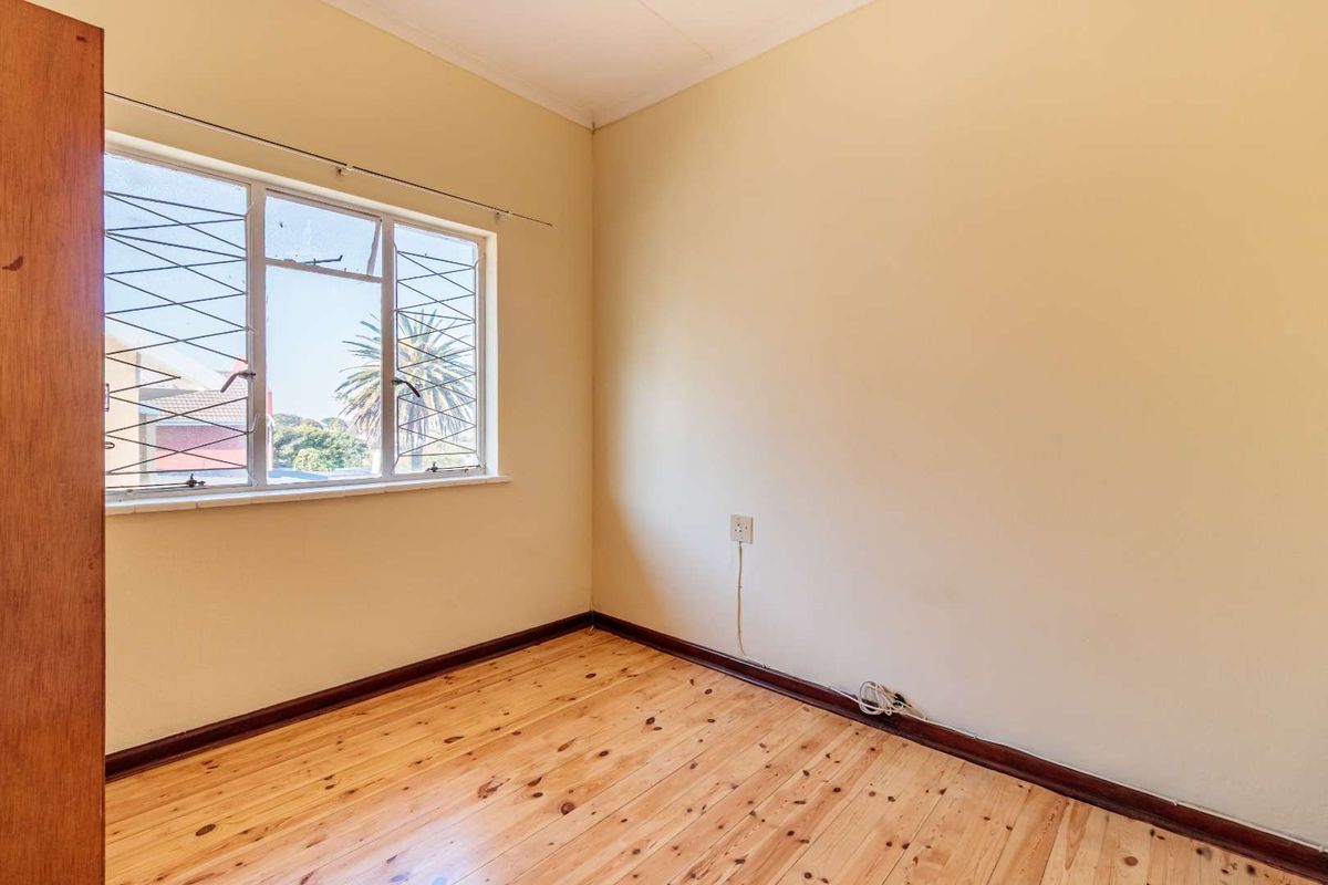 A vacant bedroom featuring polished timber flooring, neutral walls, and a window fitted with security bars.
