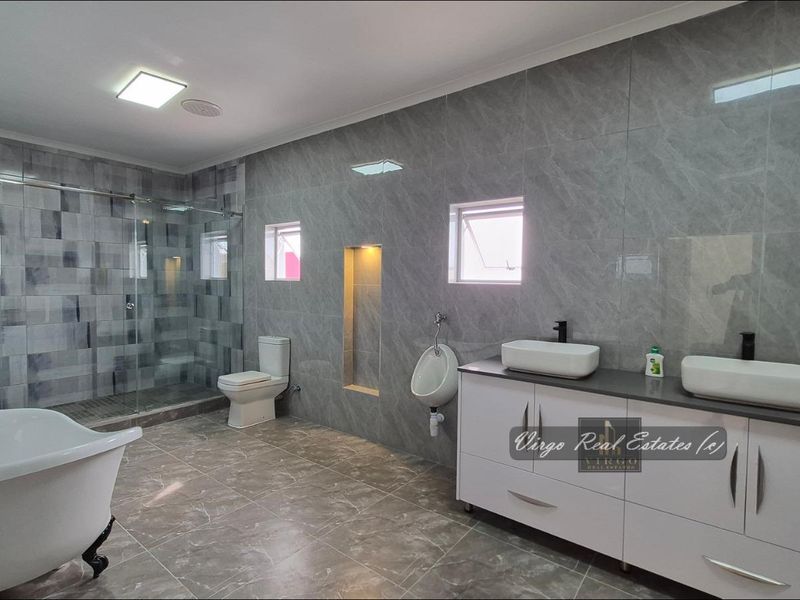 A modern, spacious bathroom featuring a freestanding bathtub, a glass-enclosed shower, a dual vanity with vessel sinks, and a wall-mounted urinal.