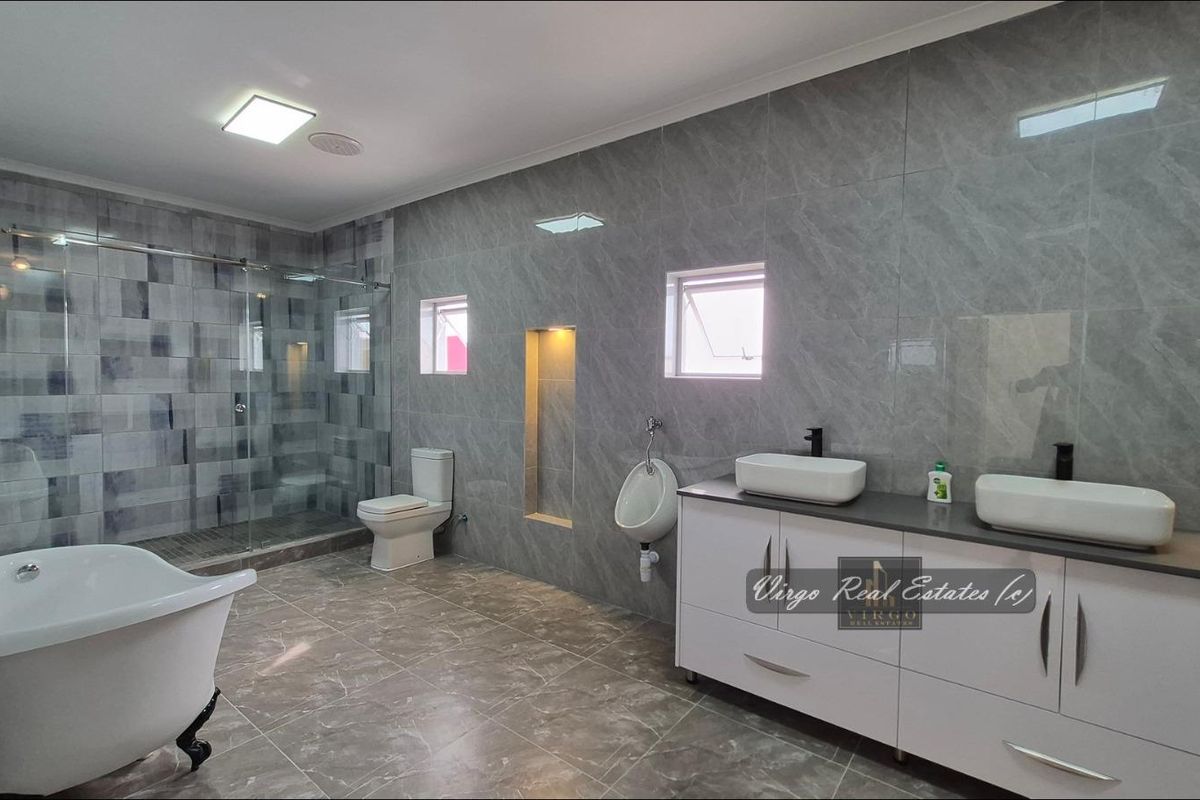 A modern, spacious bathroom featuring a freestanding bathtub, a glass-enclosed shower, a dual vanity with vessel sinks, and a wall-mounted urinal.