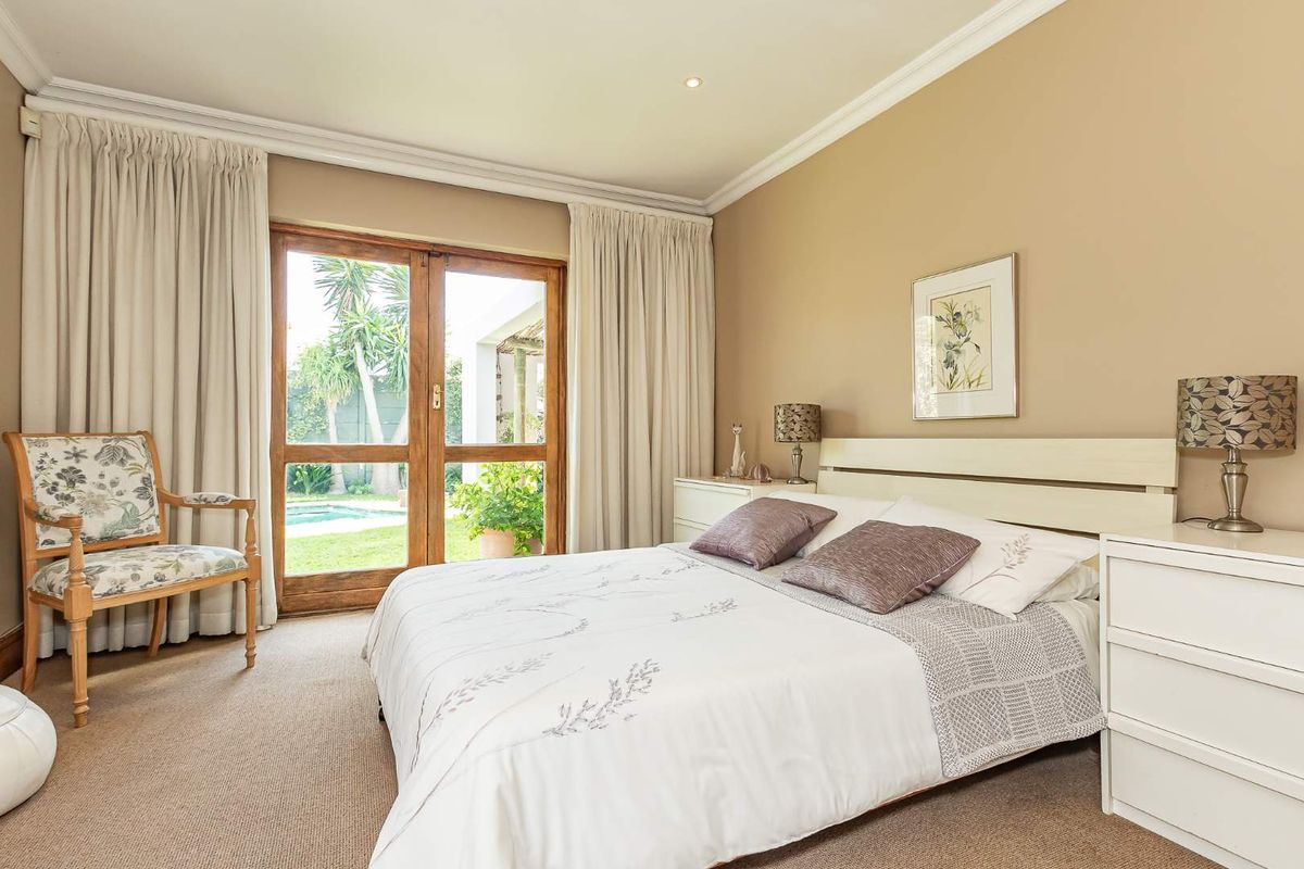 A well-maintained bedroom featuring neutral walls, crown molding, and timber-framed glass doors providing direct access to the garden and pool area.