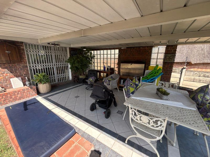 Covered outdoor patio featuring a built-in braai, brick fireplace, and tiled flooring, providing a functional space for outdoor entertaining.