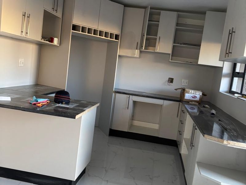 A modern, newly installed kitchen featuring white cabinetry, dark countertops, and tiled flooring, currently awaiting final appliance installation and finishing touches.