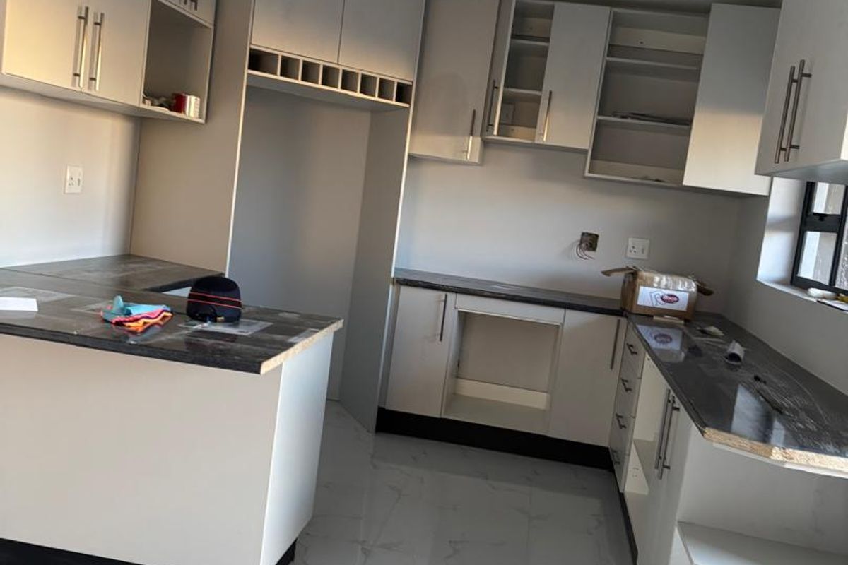 A modern, newly installed kitchen featuring white cabinetry, dark countertops, and tiled flooring, currently awaiting final appliance installation and finishing touches.