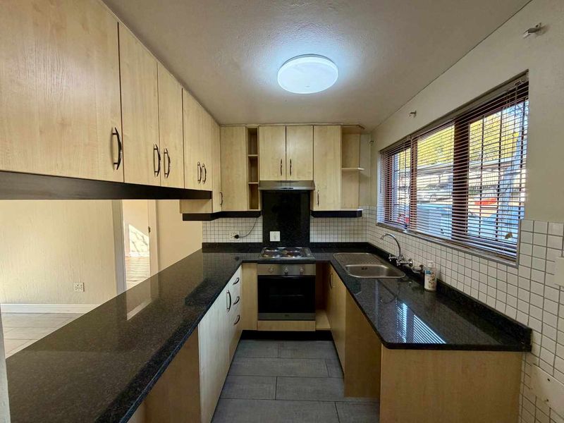 A functional kitchen featuring light wood-finish cabinetry, dark granite countertops, a built-in oven and hob, and a tiled backsplash.