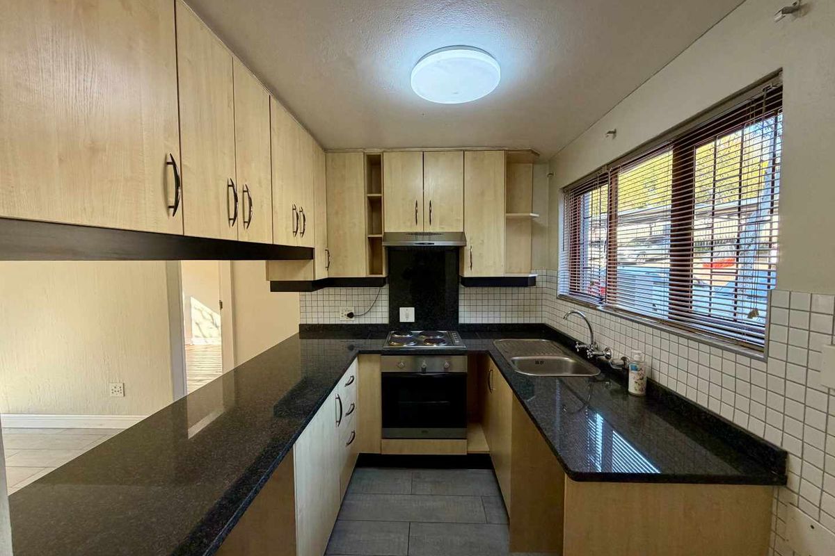A functional kitchen featuring light wood-finish cabinetry, dark granite countertops, a built-in oven and hob, and a tiled backsplash.