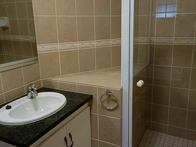 A functional bathroom featuring a vanity with granite countertop, drop-in basin, and a glass-enclosed shower with neutral wall tiling.