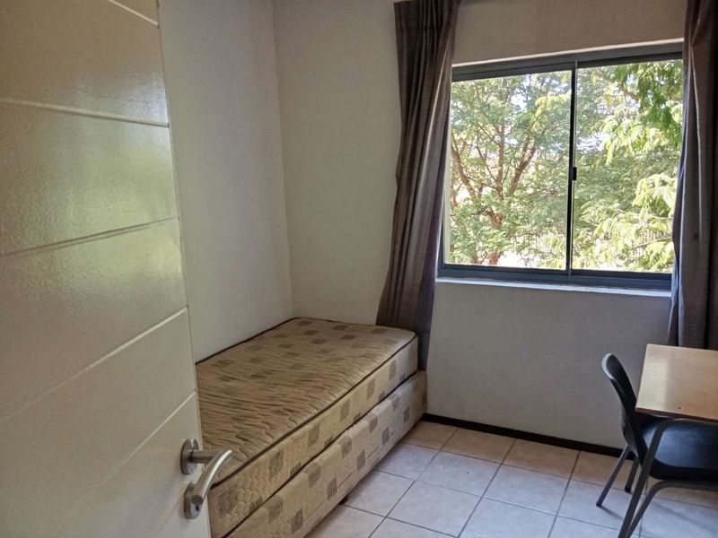 A compact bedroom featuring tiled flooring and a window with views of surrounding trees.