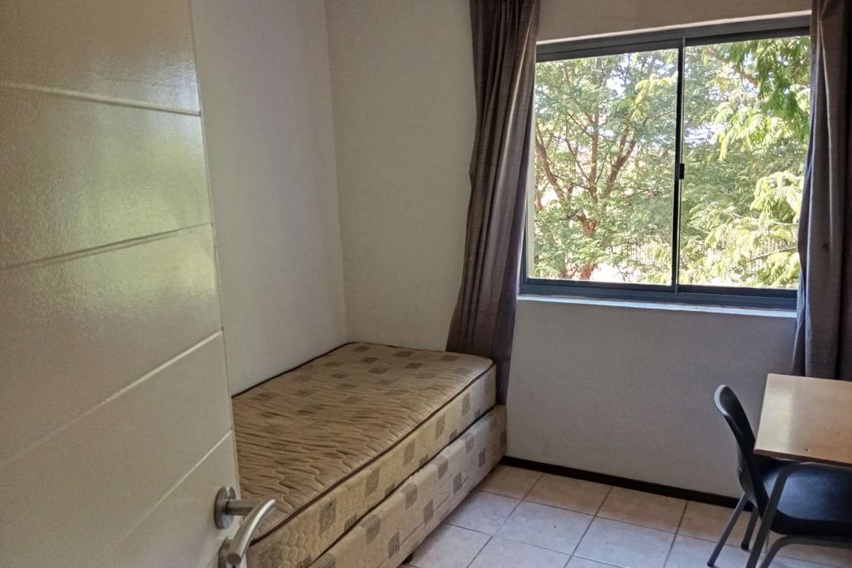 A compact bedroom featuring tiled flooring and a window with views of surrounding trees.