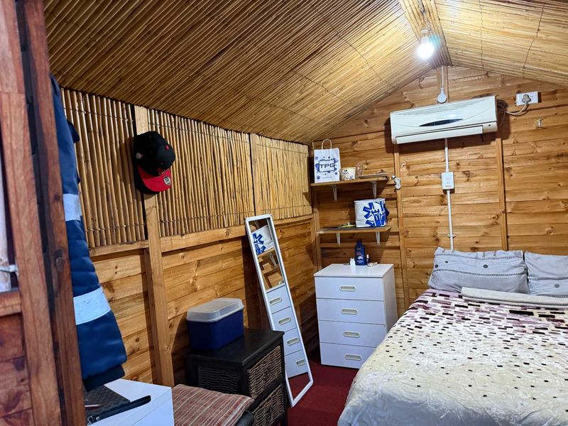 A cozy bedroom featuring timber wall paneling, a bamboo ceiling, and a wall-mounted split-system air conditioner.