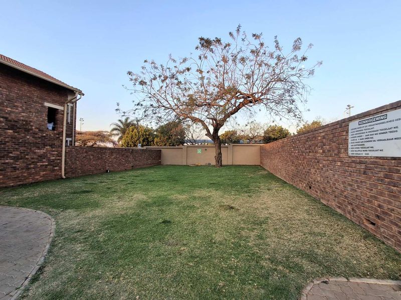 A spacious private garden area featuring a well-maintained lawn, mature tree, and secure brick boundary walls within the apartment complex.