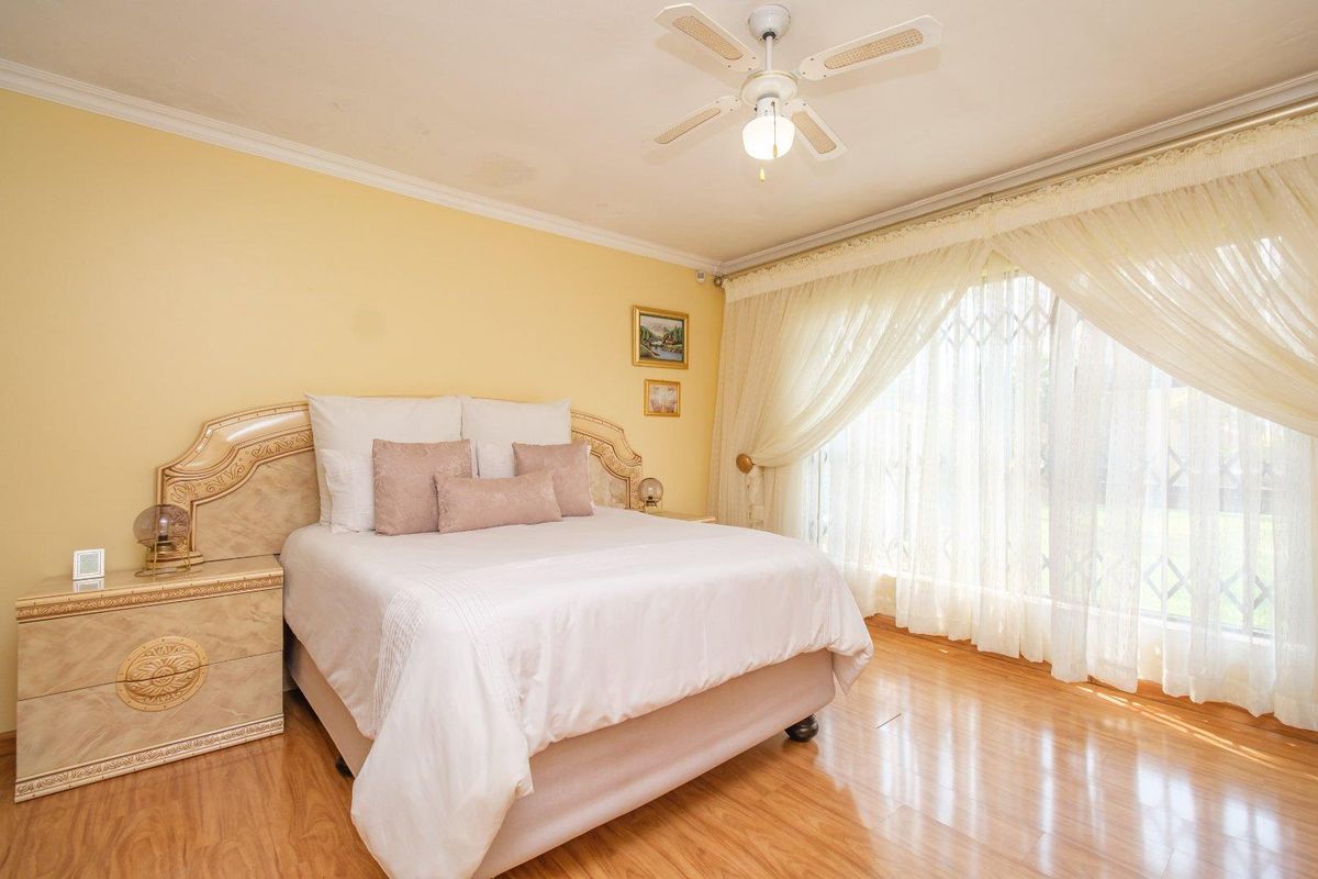 A bedroom featuring laminate flooring, a ceiling fan, and a sliding door with a security gate, showing minor ceiling water staining.