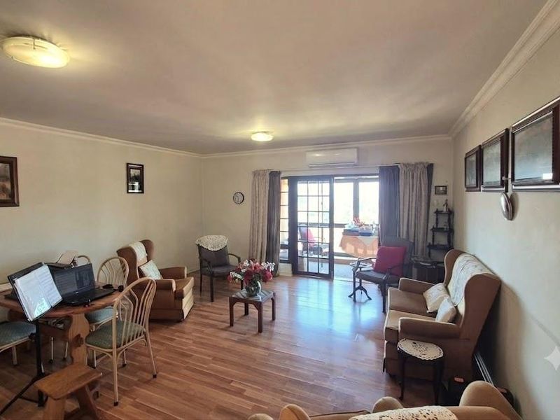 Spacious living room featuring laminate flooring, crown molding, and a split-system air conditioner, with direct access to an outdoor balcony through sliding glass doors.