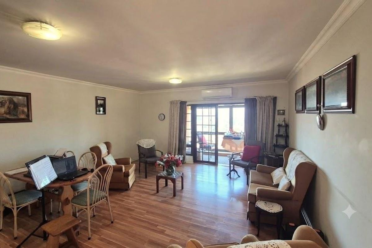 Spacious living room featuring laminate flooring, crown molding, and a split-system air conditioner, with direct access to an outdoor balcony through sliding glass doors.