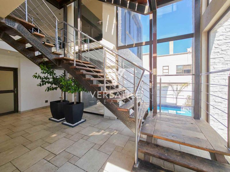 Modern entrance hall featuring an open riser staircase with stainless steel balustrades and expansive floor-to-ceiling windows overlooking the pool area.