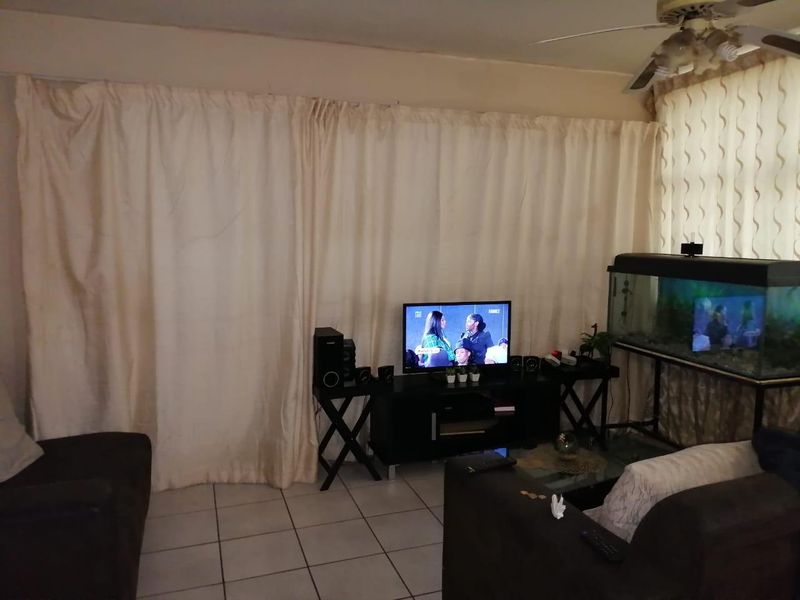 A living room area featuring tiled flooring and a ceiling fan, currently utilized as a lounge space.