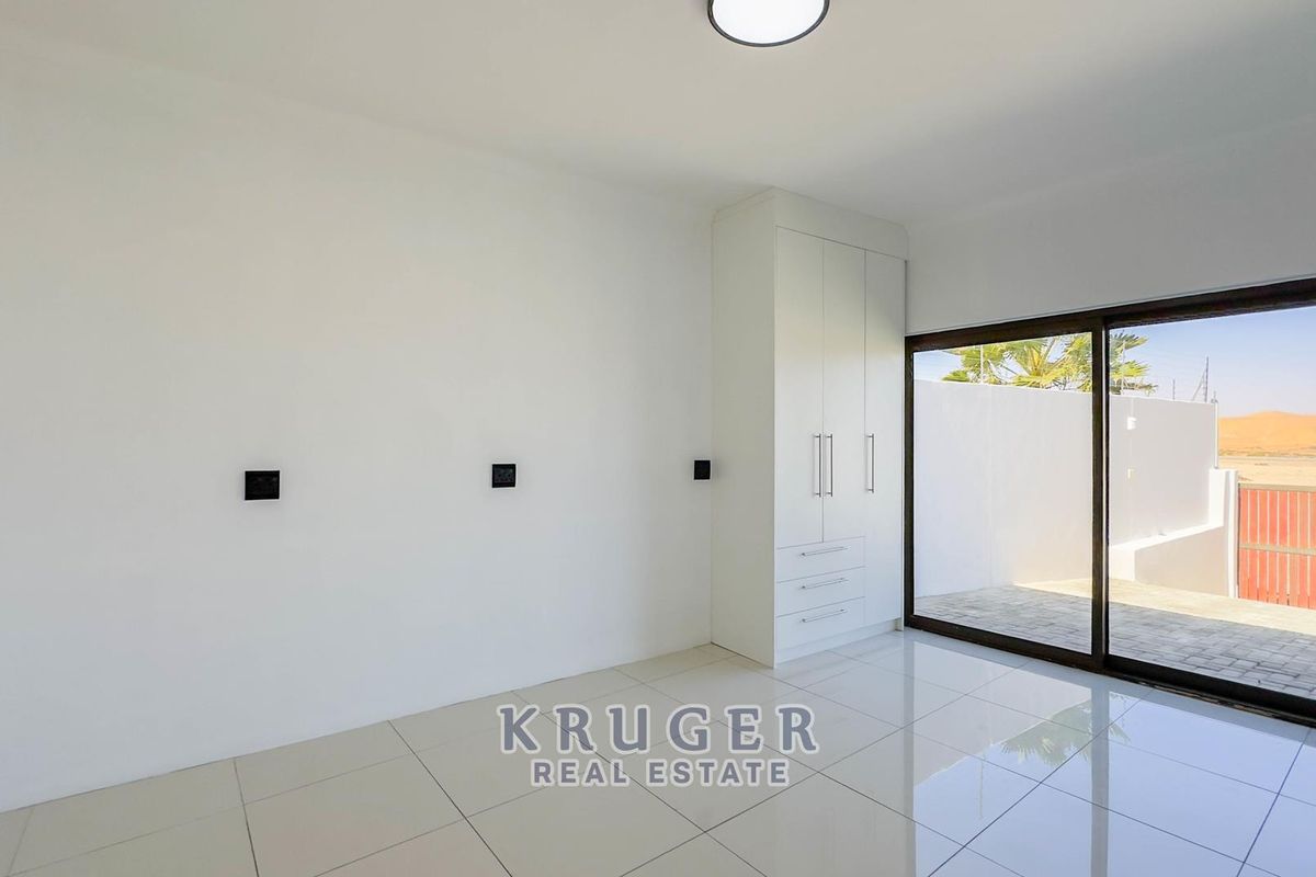 A bright, modern bedroom featuring sleek tiled flooring, built-in cabinetry, and large sliding glass doors providing direct access to an outdoor patio area.