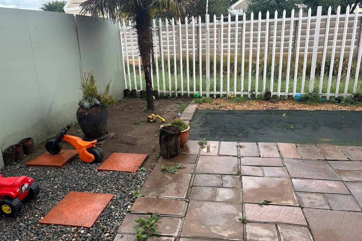 A small rear garden area featuring paved patio space, gravel sections, and perimeter fencing, currently requiring landscaping and maintenance.