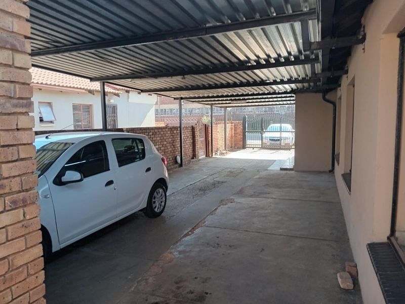 A covered carport area featuring a corrugated metal roof, brick boundary walls, and a secure metal entrance gate.