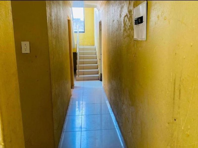 A vacant hallway featuring tiled flooring and a staircase, showing signs of wear on the wall surfaces.