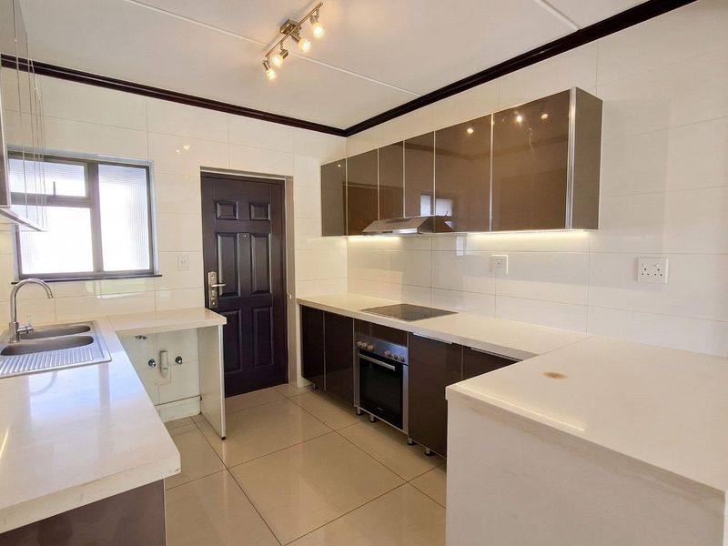 Modern kitchen featuring high-gloss cabinetry, quartz countertops, integrated appliances, and under-cabinet lighting, offering a clean and functional workspace.