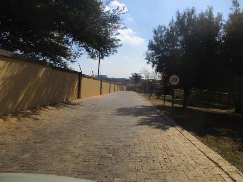 A paved driveway approach leading into the property, featuring a high perimeter wall with integrated electric fencing.