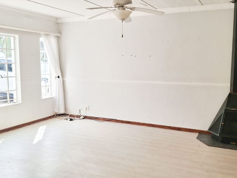 A bright, empty living room featuring a freestanding fireplace, ceiling fan, and laminate flooring, offering a blank canvas for interior design.