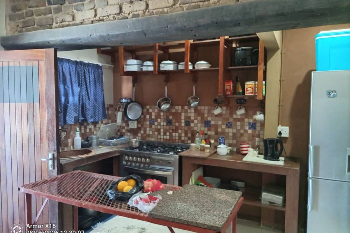 Rustic kitchen featuring exposed brickwork, wooden structural beams, gas stove, and open shelving with a tiled backsplash and concrete work surfaces.