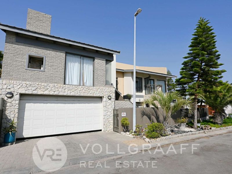 Front elevation of a modern house featuring stone cladding, a double garage, and a paved driveway with established landscaping.