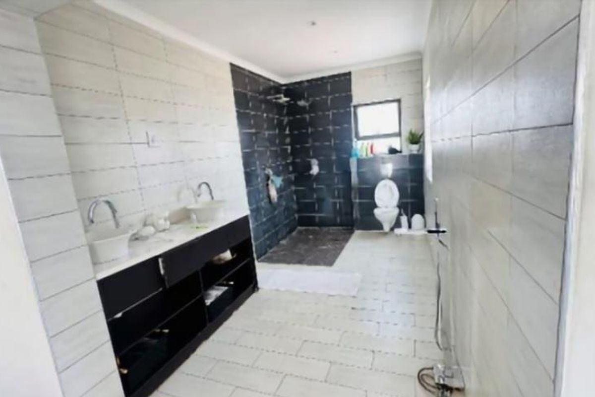 Spacious bathroom featuring a double vanity, walk-in shower, and toilet, currently undergoing finishing touches with tiling work in progress.