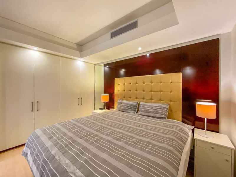 A well-maintained bedroom featuring built-in cupboards, recessed ceiling lighting, ducted air conditioning, and a modern mirrored feature wall.