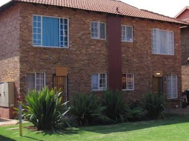 A two-story townhouse featuring a face brick exterior, tiled roof, and established garden area.