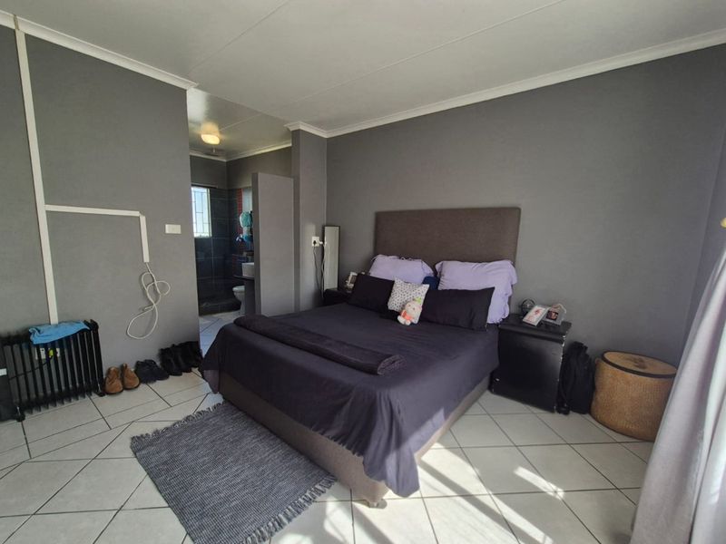 A bedroom featuring tiled flooring and an adjoining en-suite bathroom, with neutral grey wall finishes and standard ceiling cornicing.