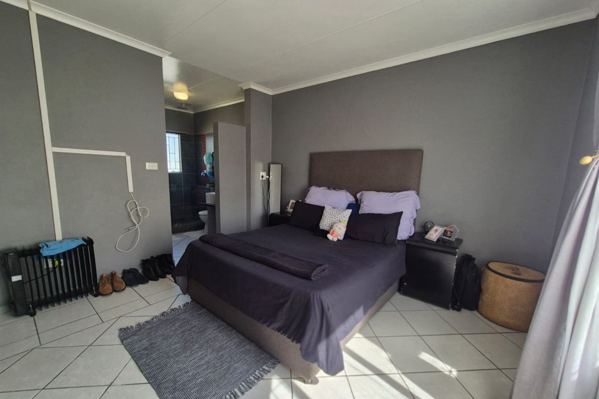 A bedroom featuring tiled flooring and an adjoining en-suite bathroom, with neutral grey wall finishes and standard ceiling cornicing.