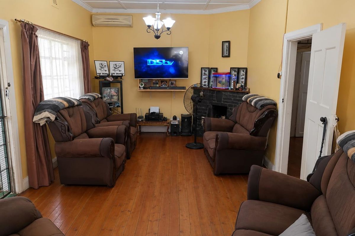A living room featuring hardwood flooring, a stone fireplace, and an air conditioning unit, offering a traditional layout with potential for modernization.