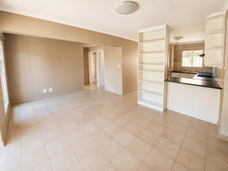 Spacious open-plan living area featuring neutral tiled flooring, a built-in shelving unit, and a functional kitchen with gas hob and ample cabinetry.