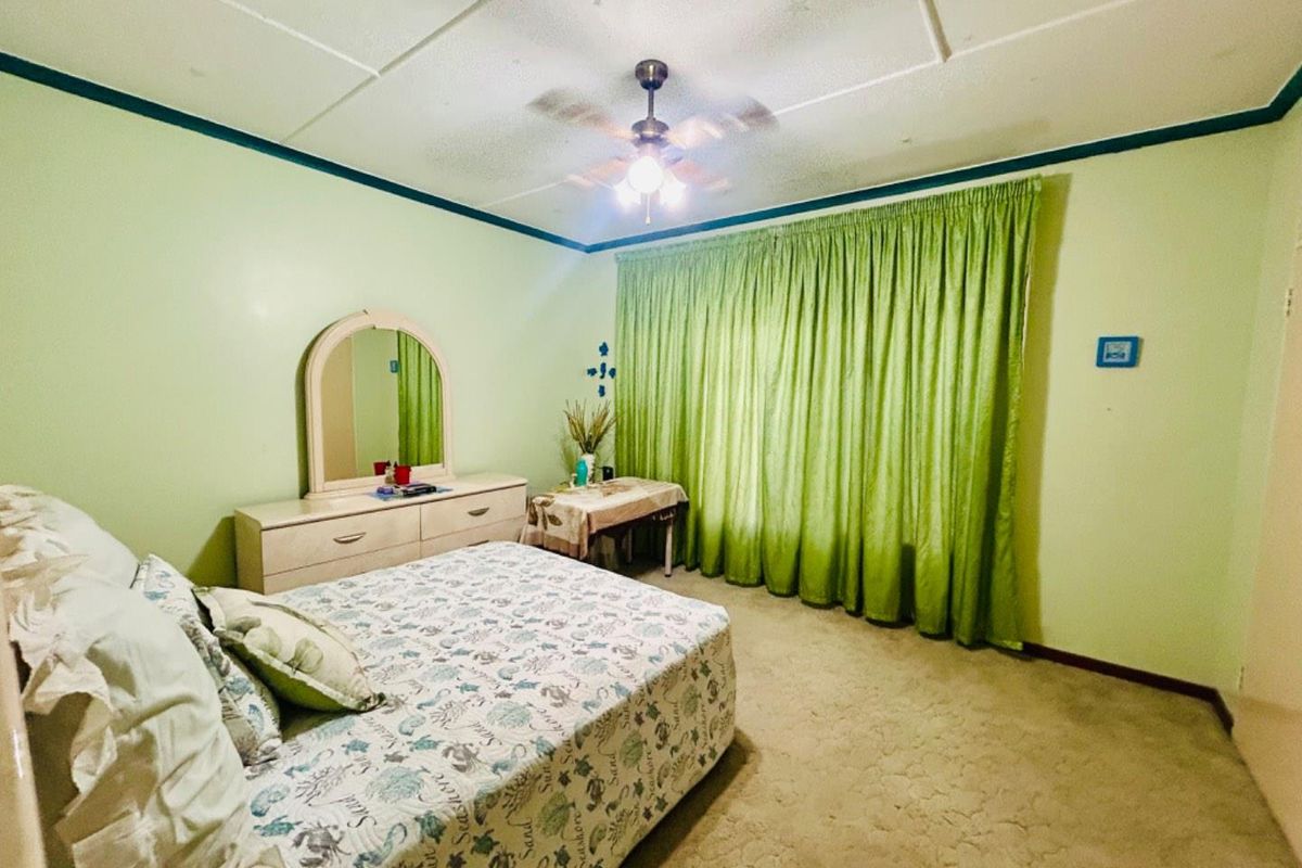 A bedroom featuring a ceiling fan, carpeted flooring, and large window curtains, offering a dated aesthetic ready for modernization.