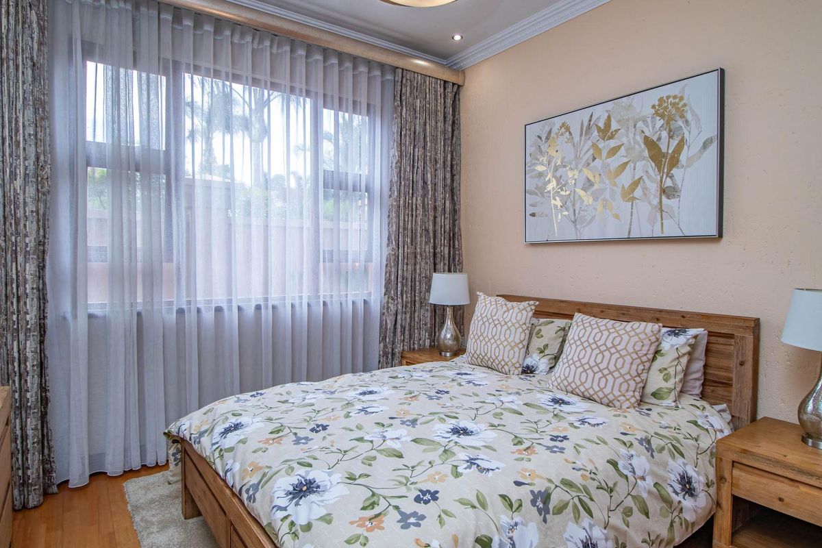 A well-maintained bedroom featuring warm-toned walls, timber flooring, and large windows dressed with floor-to-ceiling curtains.