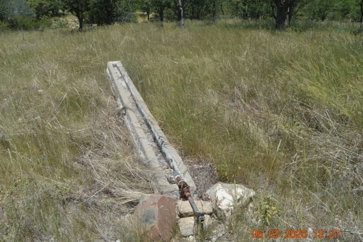 An outdoor area featuring a weathered concrete water trough with exposed metal piping set within a grassy field.