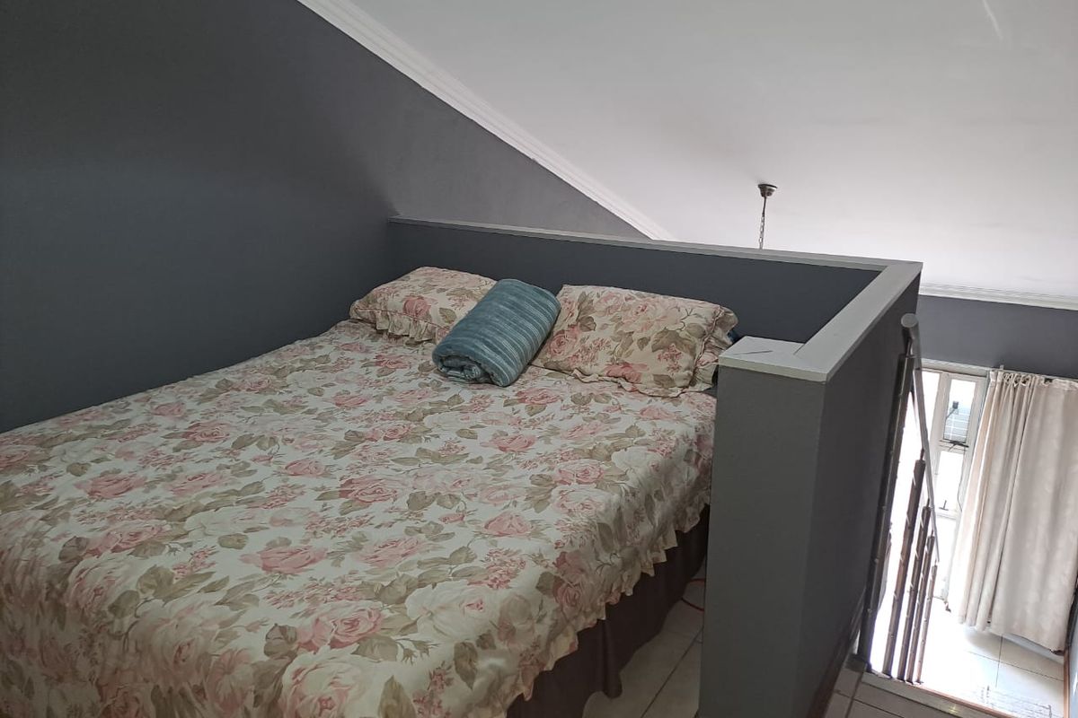 A cozy loft bedroom area featuring a sloped ceiling, dark grey accent walls, and tiled flooring, overlooking the lower level via a half-wall partition.