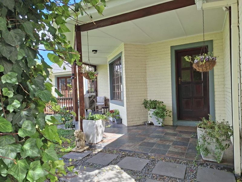 A covered patio area featuring tiled flooring, timber support beams, and a classic timber panelled entrance door with painted brick exterior walls.