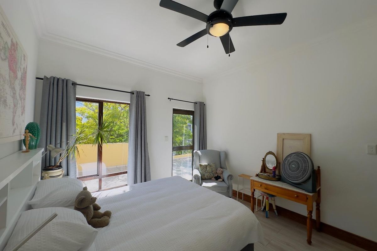 A bright bedroom featuring a ceiling fan, light-toned flooring, and direct access to an outdoor balcony through glass doors.