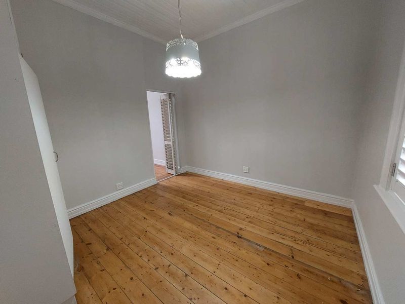 A bright, empty bedroom featuring polished timber flooring, neutral walls, and classic shutter blinds, offering a clean canvas for personalization.