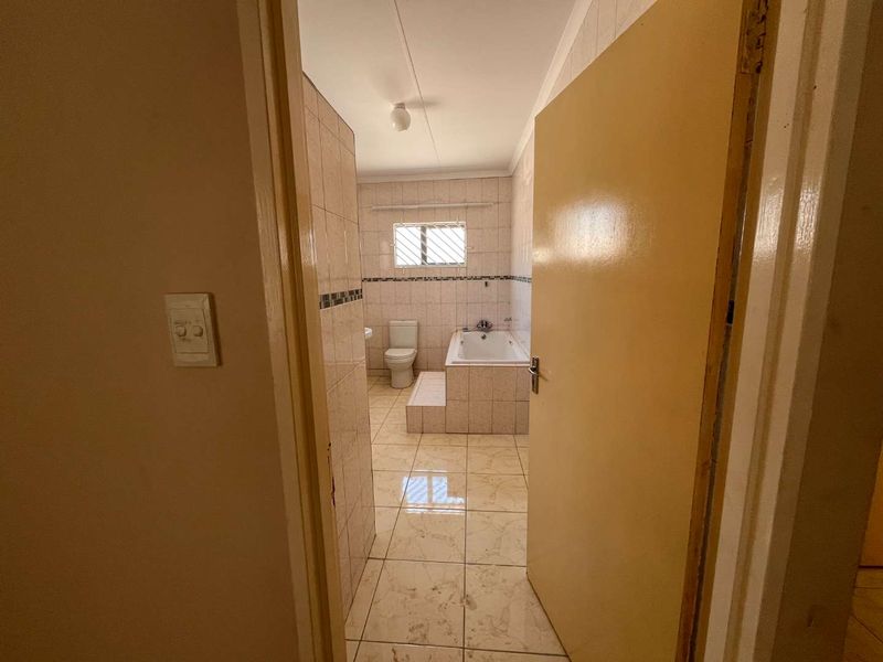 A functional bathroom featuring tiled walls and flooring, a built-in bathtub, and a toilet, presented in a clean, empty state.